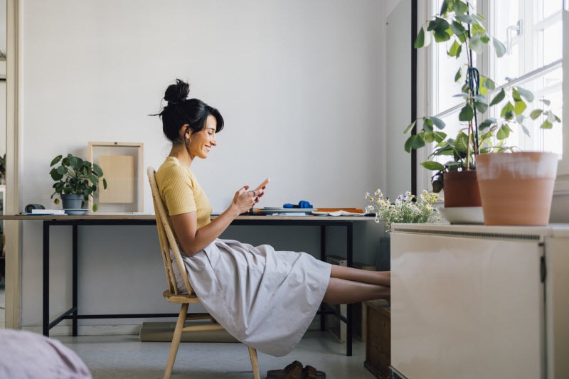 Concept of ADHD in Women Represented by Woman Sitting at Desk With Feet Up Distracted by Her Phone