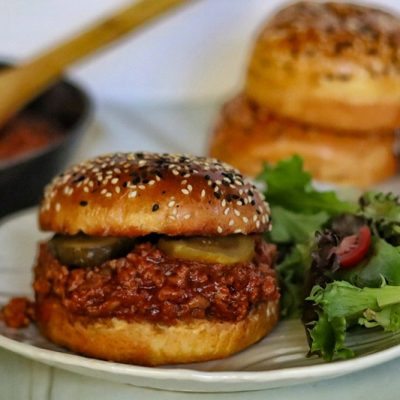 A Turkey Sloppy Joe With Pickes and a Sesame Seed Bun is Served With Salad.