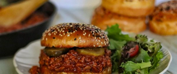A Turkey Sloppy Joe With Pickes and a Sesame Seed Bun is Served With Salad.
