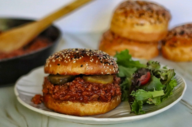 A Turkey Sloppy Joe With Pickes and a Sesame Seed Bun is Served With Salad.
