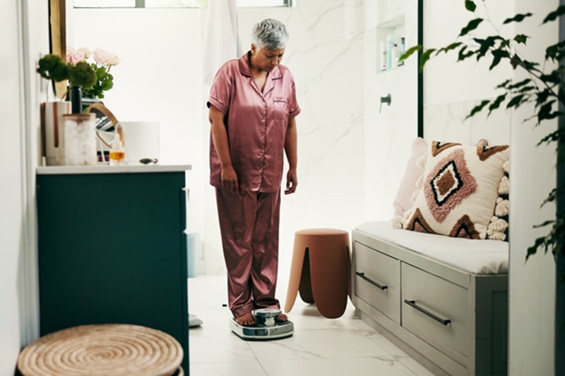 Unexplained Weight Gain A Woman Stands on a Bathroom Scale and Looks Down at the Number, Representing Unexplained Weight Gain