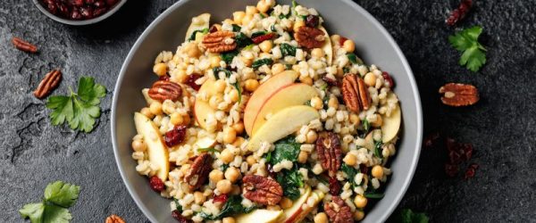 Pearl Barley, Kale & Apple Salad with Pecan Halves in Big Bowl on Slate Countertop Dotted with Cranberries and Pecan Halves