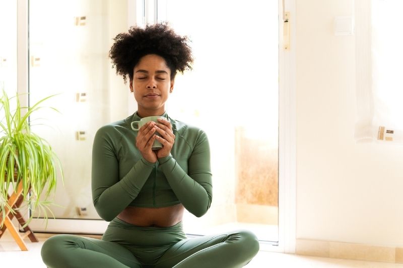 What Are the Doshas Woman Meditating in Green Activewear While Holding a Cup Indoors
