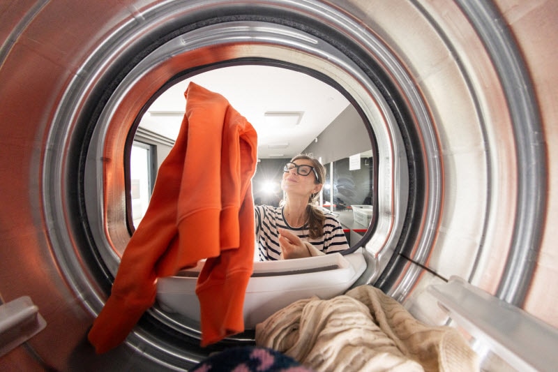 Woman Taking Orange Sweater Out of Dryer to Represent Concept of Why You Should Wash New Clothes Before Wearing
