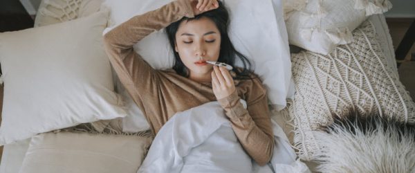 Your Cold and Flu Strategy - Focus on Gut Health and Immunity Overhead View of Ill Woman in Bed Taking Her Temperature to Represent Concept of Gut Health and Immunity