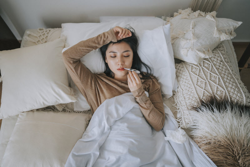 Overhead View of Ill Woman in Bed Taking Her Temperature to Represent Concept of Gut Health and Immunity