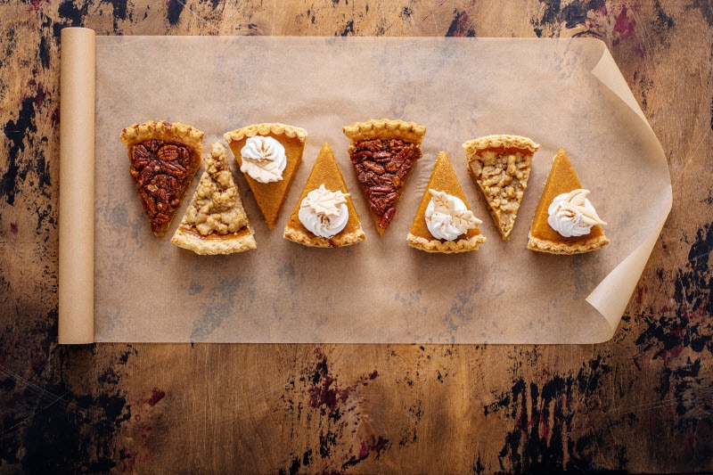 7 Tips for a Stress-Free Thanksgiving Concept of Stress-Free Thanksgiving Represented by Row of Pie Slices on Parchment Paper on Wooden Table