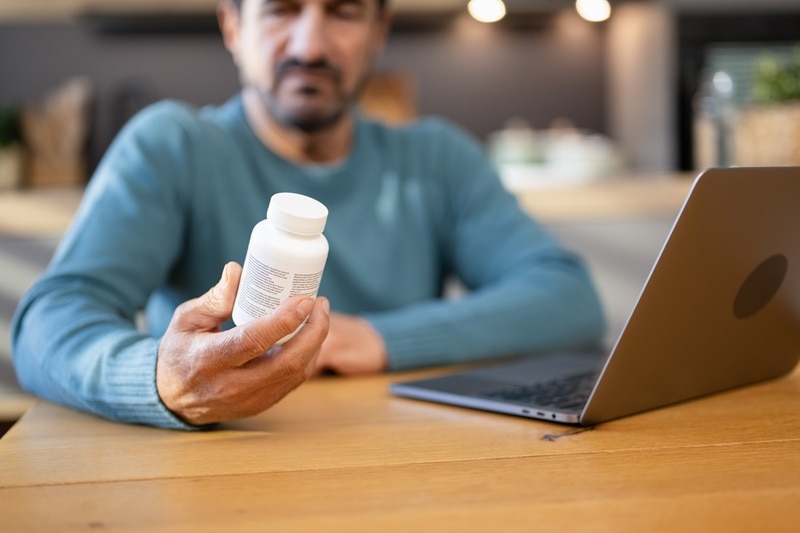 A Man Examines the Label on a Supplement Bottle, Representing the Best Supplements for Diabetes.