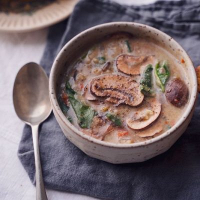 Wild Rice Soup With Mushrooms and Spinach in an Earthenware Bowl With Golden Cornbread Next to it on a Linen Napkin