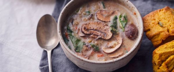Wild Rice Soup With Mushrooms and Spinach in an Earthenware Bowl With Golden Cornbread Next to it on a Linen Napkin