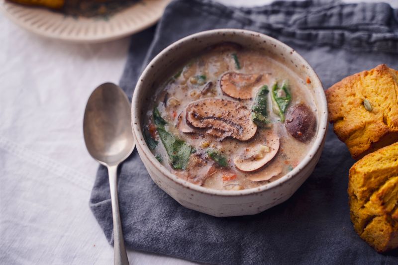 Wild Rice Soup With Mushrooms and Spinach in an Earthenware Bowl With Golden Cornbread Next to it on a Linen Napkin