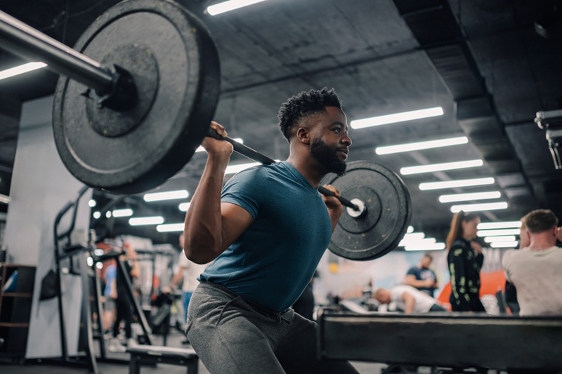 A Man Performs a Back Squat in a Gym, Representing the Question, "Does Lifting Weights Lower Blood Pressure?"