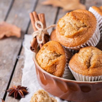 Fresh-Milled Banana Pumpkin Muffins in Rustic Crock-Type Bowl on an Outdoor Wooden Table with Fallen Leaves