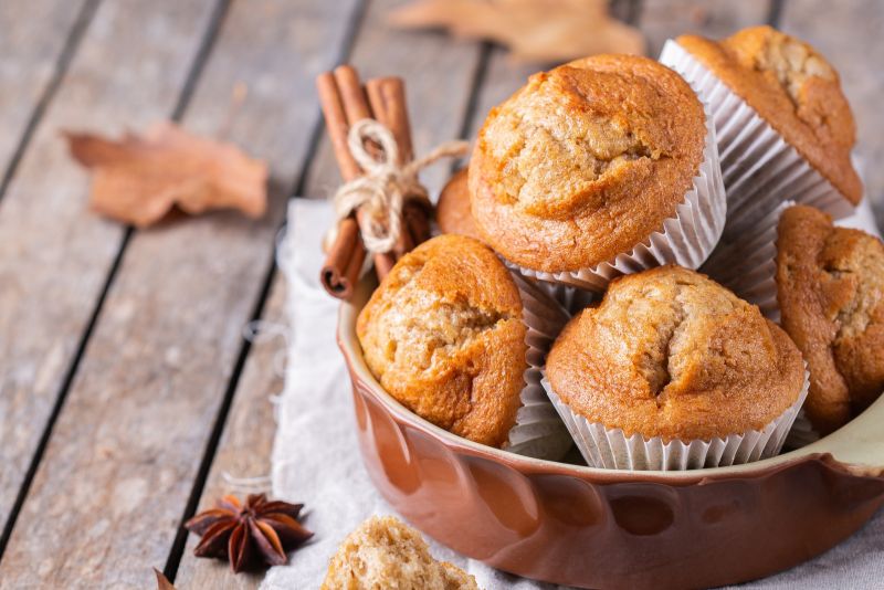 Fresh-Milled Banana Pumpkin Muffins in Rustic Crock-Type Bowl on an Outdoor Wooden Table with Fallen Leaves