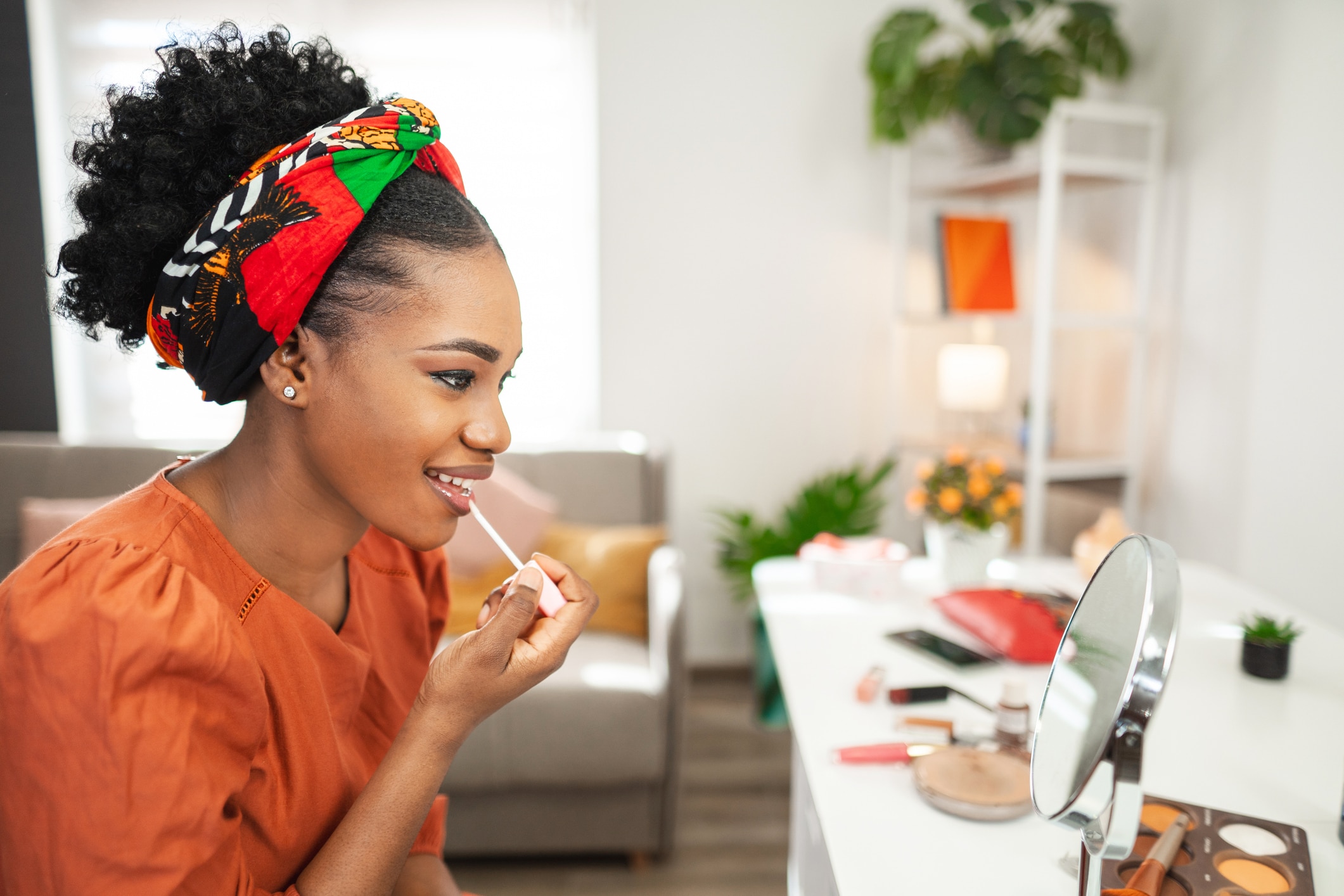 Beautiful black woman looking in the mirror while applying lipstick on her lips