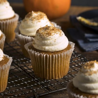 Pumpkin Muffins With Cream Cheese Frosting on Cooling Rack with a Pumpkin on the Table in the Background