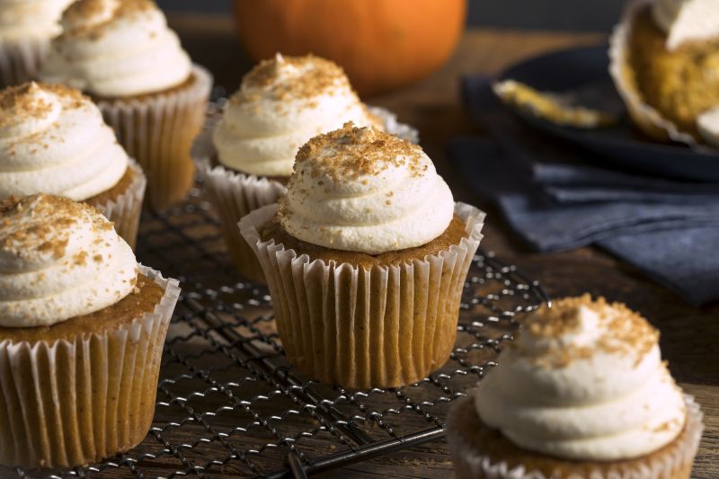 Pumpkin Muffins With Cream Cheese Frosting on Cooling Rack with a Pumpkin on the Table in the Background