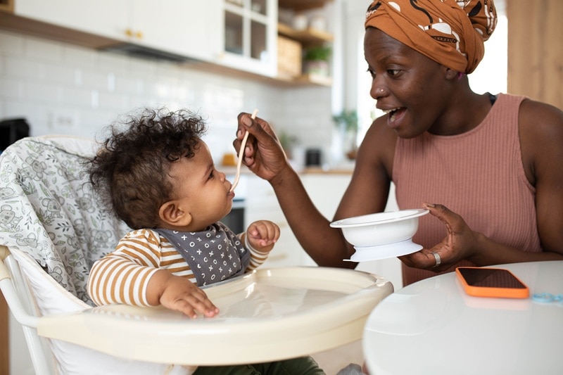 A Mother Spoon Feeds Her Infant Baby, Representing How to Introduce Allergens to Baby.