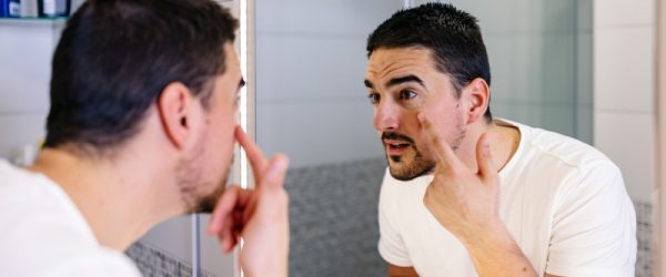 A Man Examines His Skin in the Mirror, Representing How to Repair Skin Barrier.