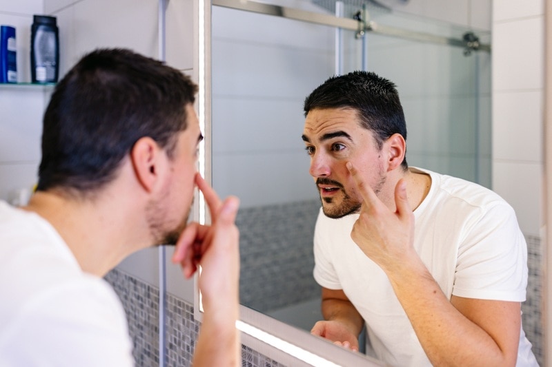 A Man Examines His Skin in the Mirror, Representing How to Repair Skin Barrier.