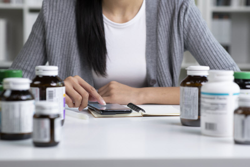 Is it OK to Take Expired Vitamins Torso View of Woman at Desk Researching Supplements on Phone Trying to Find Out Is it OK to Take Expired Vitamins