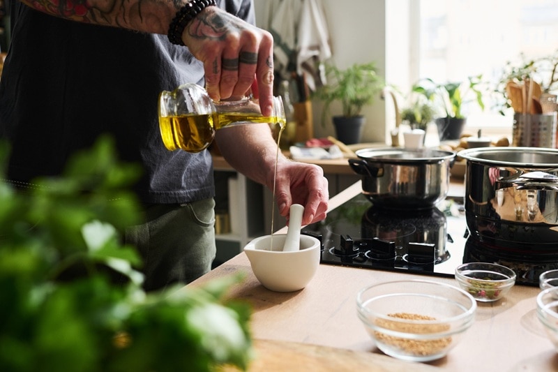 A Man Pours Olive Oil Into a Small Mortar While Cooking, Representing Olive Oil Shots.