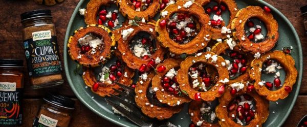 Roasted Delicata Squash With Feta & Pomegranate_Resized Image_Frontier Co-op Circles of Roasted Delicata Squash Sprinkled With Feta Cheese and Pomegranate Seeds on an Oval Serving Platter Next to Bottles of Frontier Co-op Spices