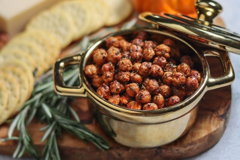 Roasted Rosemary-Infused Crispy Chickpeas in Metal Serving Pot on Charcuterie Board with Crackers, Veggies and Rosemary Sprigs