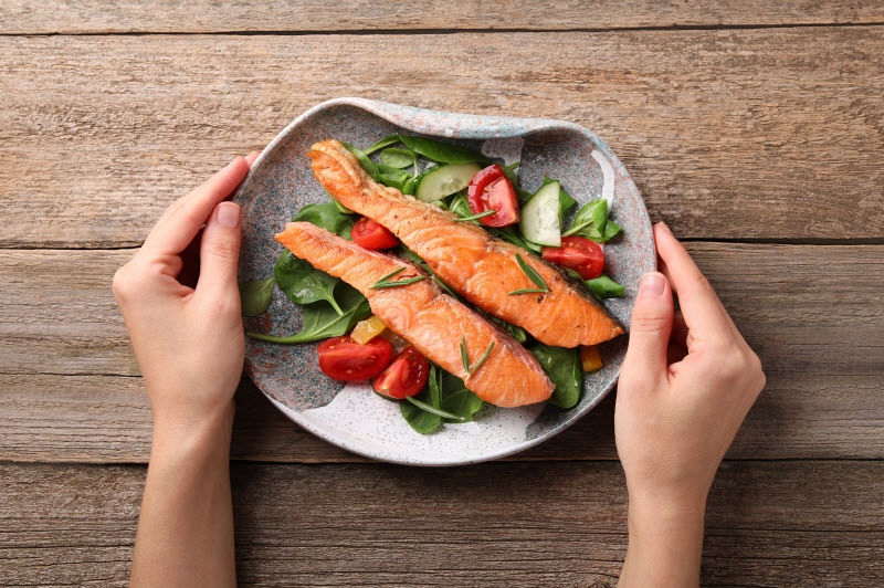 Woman's' Hands Holding Plate of Salmon and Vegetables to Represent Concept of Omega-3 and Brain Health