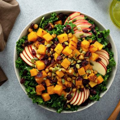Thanksgiving salad in big bowl with caramelized butternut squash, sliced apples, kale and cranberries tossed in a creamy maple-mustard dressing