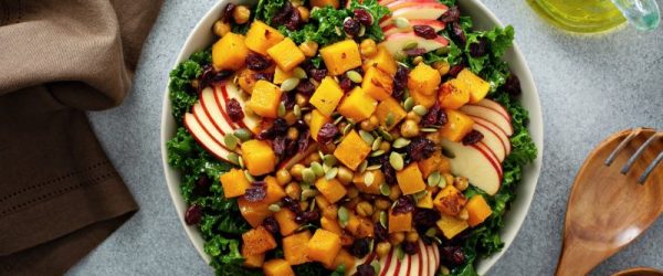 Thanksgiving salad in big bowl with caramelized butternut squash, sliced apples, kale and cranberries tossed in a creamy maple-mustard dressing