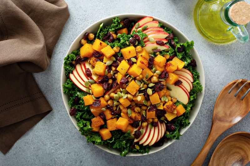 Thanksgiving salad in big bowl with caramelized butternut squash, sliced apples, kale and cranberries tossed in a creamy maple-mustard dressing