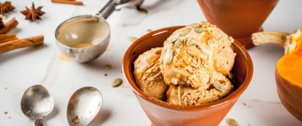 Vegan Pecan Pumpkin Pie Ice Cream_Resized Image_Liana Vegan Pecan Pumpkin Pie Ice Cream in Serving Dish With Pumpkin Seeds Sprinkled on Top, Spoons and an Ice Cream Scoop Adorn the Counter