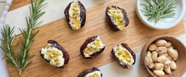 Vegan Stuffed Dates Vegan Stuffed Medjool Dates With Rosemary Tofu Ricotta, Hot Agave “Honey,” and Chopped Pistachios Arranged on a Wooden Serving Board With Fresh Rosemary and Pistachios