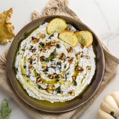 Walnut and Feta Dip in a Big Appetizer Bowl On a Marble Counter Strewn with Fall Leaves and a Decorative Pumpkin