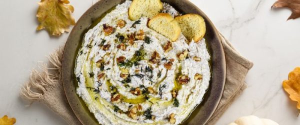 Walnut and Feta Dip in a Big Appetizer Bowl On a Marble Counter Strewn with Fall Leaves and a Decorative Pumpkin