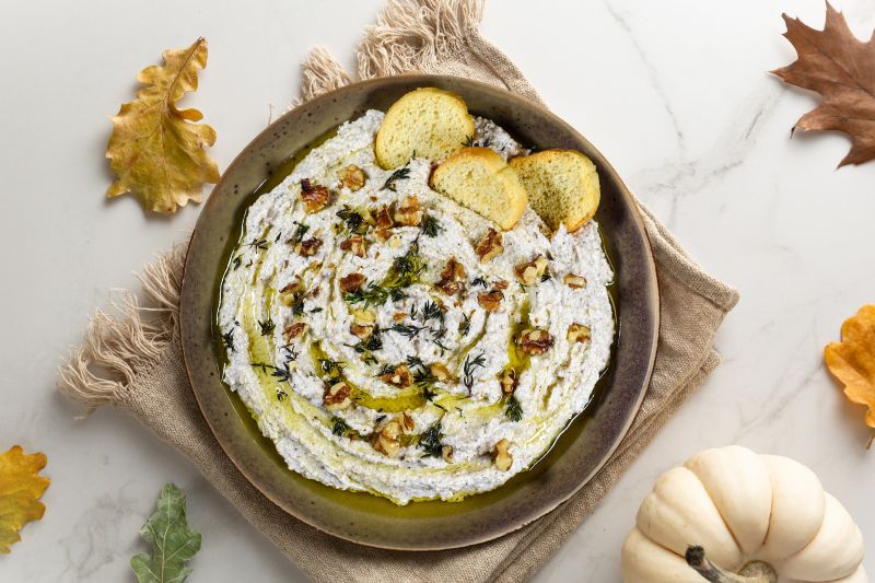 Walnut and Feta Dip in a Big Appetizer Bowl On a Marble Counter Strewn with Fall Leaves and a Decorative Pumpkin