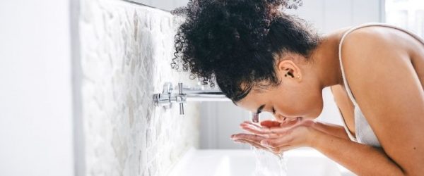 What Is Double Cleansing Woman Double Cleansing Her Face With Water at a Bright, Modern Bathroom Sink
