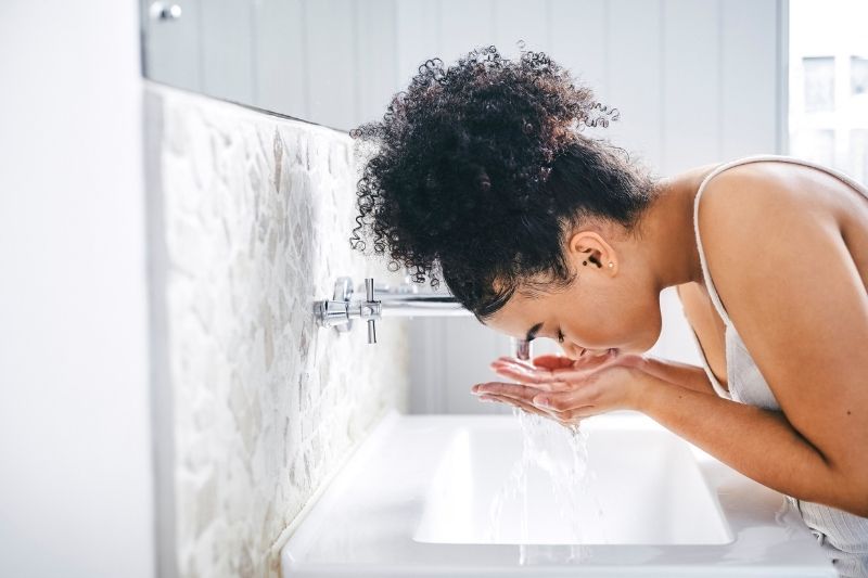 Woman Double Cleansing Her Face With Water at a Bright, Modern Bathroom Sink