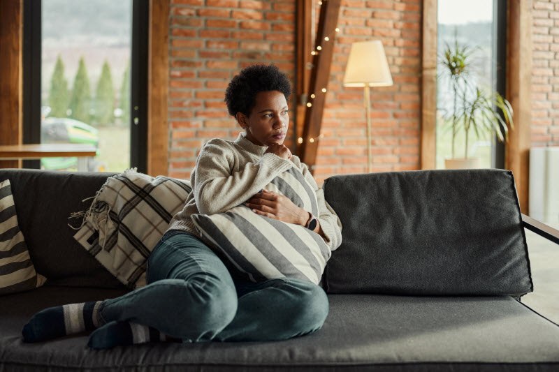 Woman Sitting on Couch Looking Off Into Distance Worrying About What Is Inflammaging and is it Affecting Her?