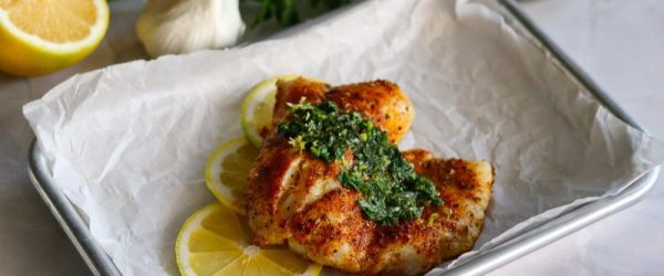 Baked Cod With Gremolata Sauce_Resized Image_Toni Williams Seasoned Baked Cod Drizzled With Gremolata Sauce on a Sheet Pan Surrounded by Lemon Slices and a Bulb of Fresh Garlic