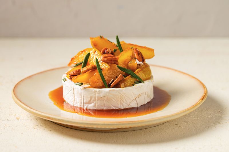 A Wheel of Brie on a Plate With Caramelized Pears & Toasted Walnuts all Nestled in a Pool of Caramelized Sugar