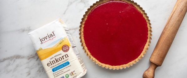 A Bright Red Cranberry Orange Tart Sits Beside a Bag of Einkorn Flour and a Large Wooden Rolling Pin.