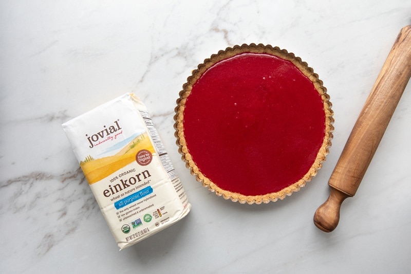 A Bright Red Cranberry Orange Tart Sits Beside a Bag of Einkorn Flour and a Large Wooden Rolling Pin.