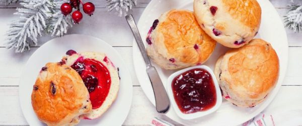 Cranberry Scones_Resized Image_Pam Higgins Fresh cranberry scones with jam on round white plates. Top view table scene on a white wood background. Christmas fur tree boughs and red berries are scattered about.