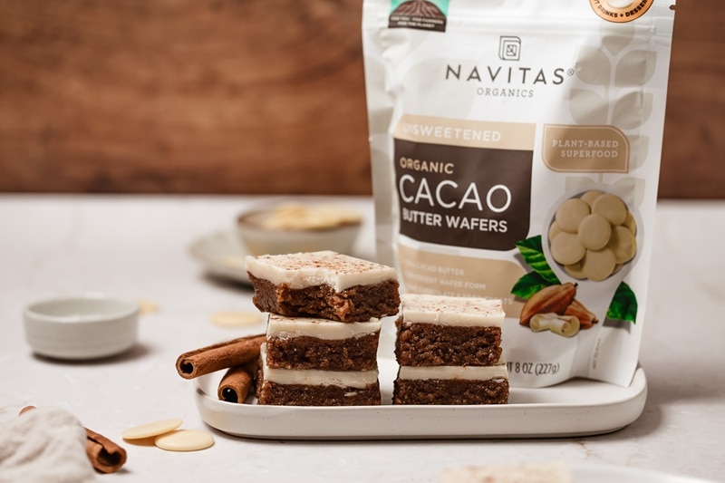 Gingerbread No Bake Cookie Dough Bars A Platter of Gingerbread No Bake Cookie Dough Bars Sits Beside a Package of Navitas Organics Cacao Butter Wafers.
