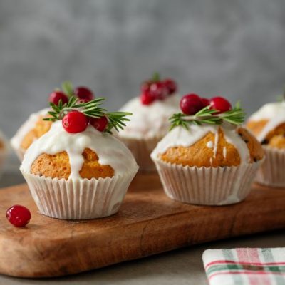 Holiday Spice Muffins with Dripping Icing Topped with Cranberries and Sprigs of Rosemary Set Atop a Wooden Serving Board