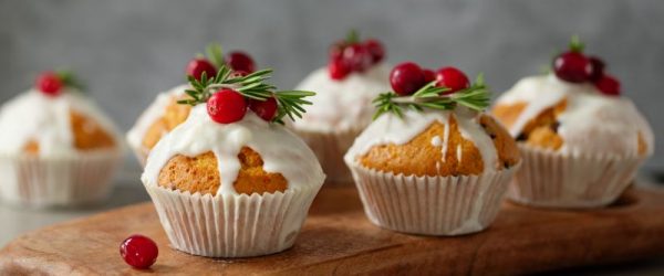 Holiday Spice Muffins with Dripping Icing Topped with Cranberries and Sprigs of Rosemary Set Atop a Wooden Serving Board