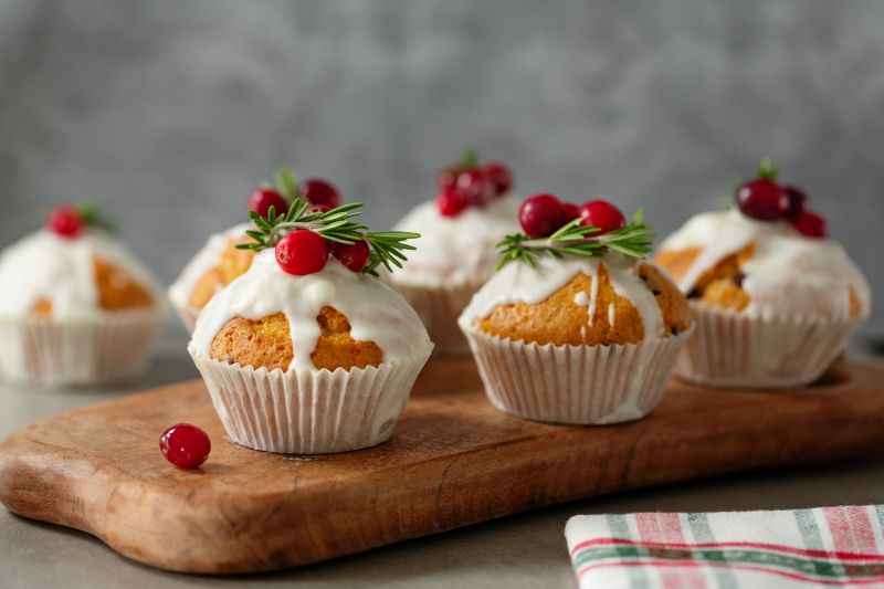 Holiday Spice Muffins with Dripping Icing Topped with Cranberries and Sprigs of Rosemary Set Atop a Wooden Serving Board