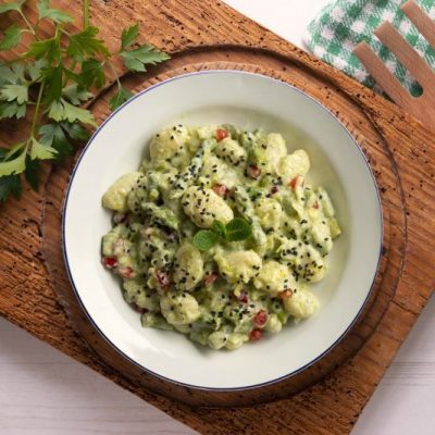 Gnocchi in Yogurt-Asparagus Cream Sauce Dotted with Pomegranate Arils on Bowl on Wooden Tray